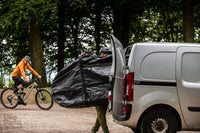 Cyclist packing muddy bike into BikeParka RoughSac for transport in van