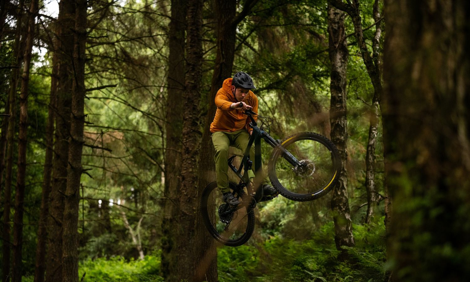 Mountain biker mid-air on a forest trail